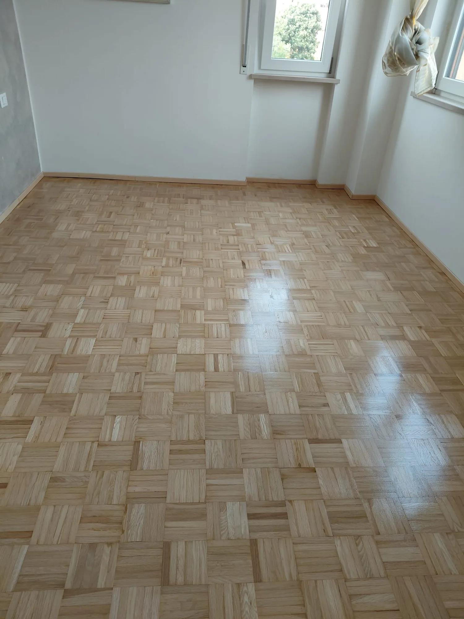 Parquet a mosaico chiaro finito, con la luce della finestra che si specchia sul legno
