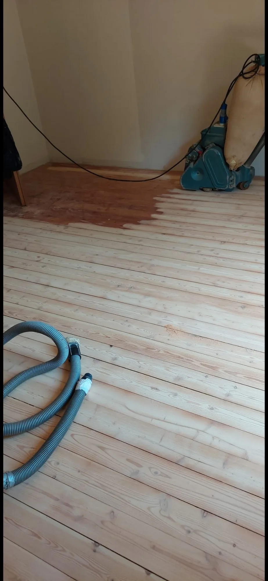 Listoni di abete levigati, con la levigatrice e il tubo dell'aspirazione in un angolo