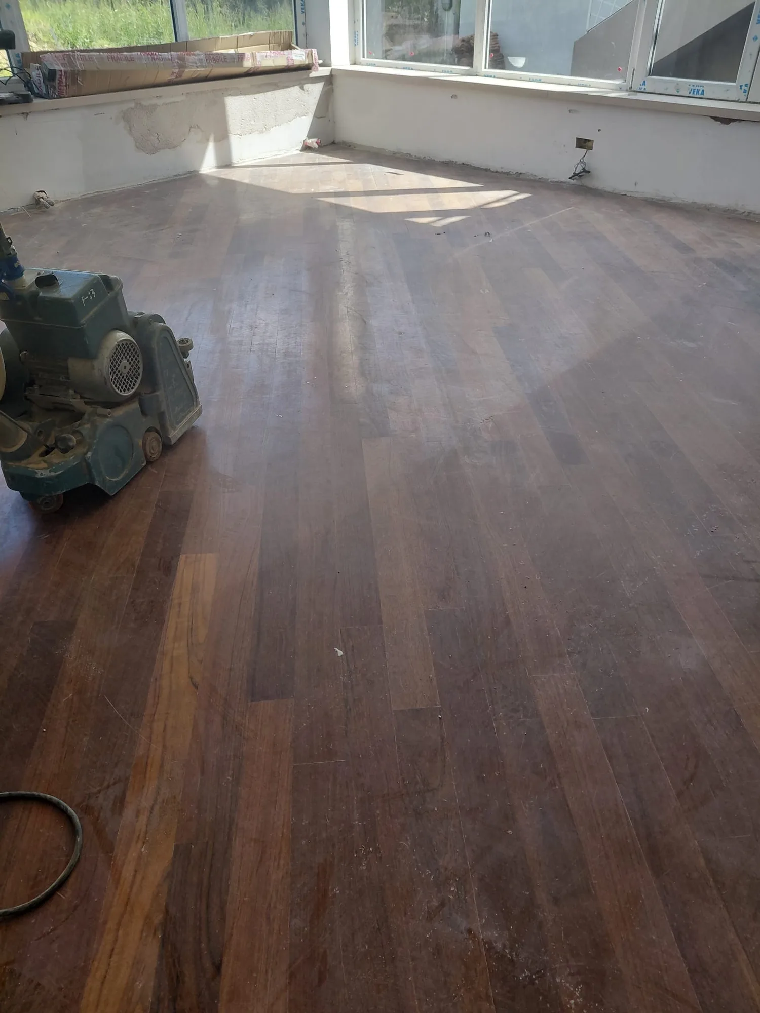 Listoni di parquet scuro segnati dal tempo con la levigatrice pronta a partire